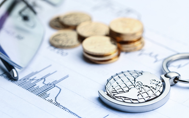 Coins, paper money, and a globe placed on a white statistics chart.