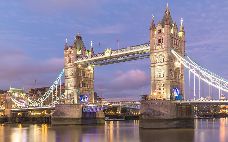 Tower Bridge illuminated at dusk, surrounded by city lights and buildings in London.
